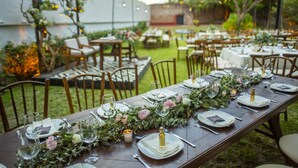 An outdoor dining area with tables set for a meal, surrounded by chairs and greenery. - Hotel Boutique Hacienda del Gobernador (Colima)
