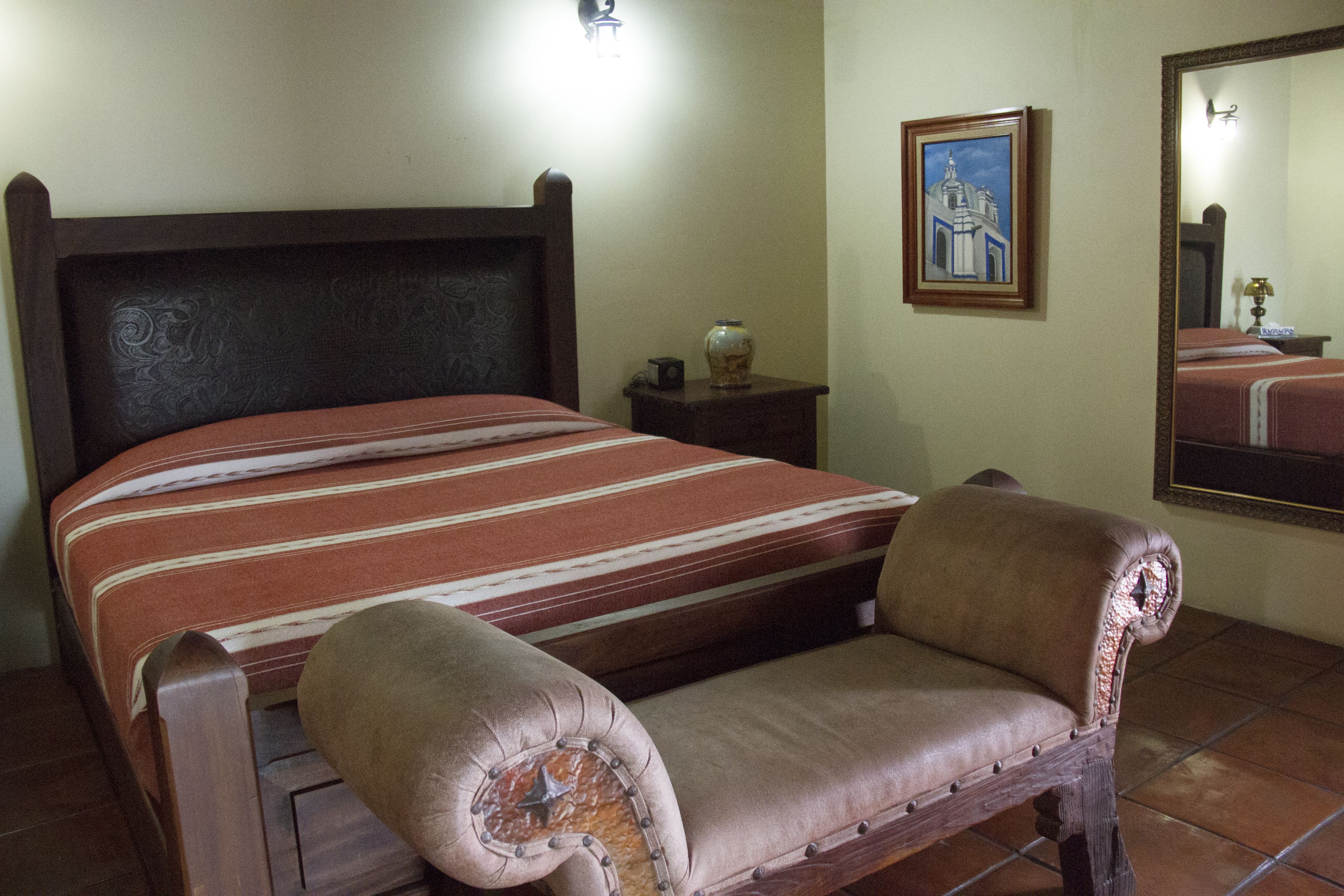 A bed with a striped bedspread, a wooden headboard, a nightstand with a vase, and a framed picture on the wall.