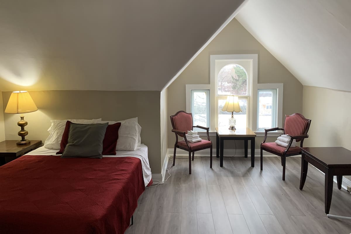 Une chambre à coucher avec un lit, deux chaises, une table et une lampe.