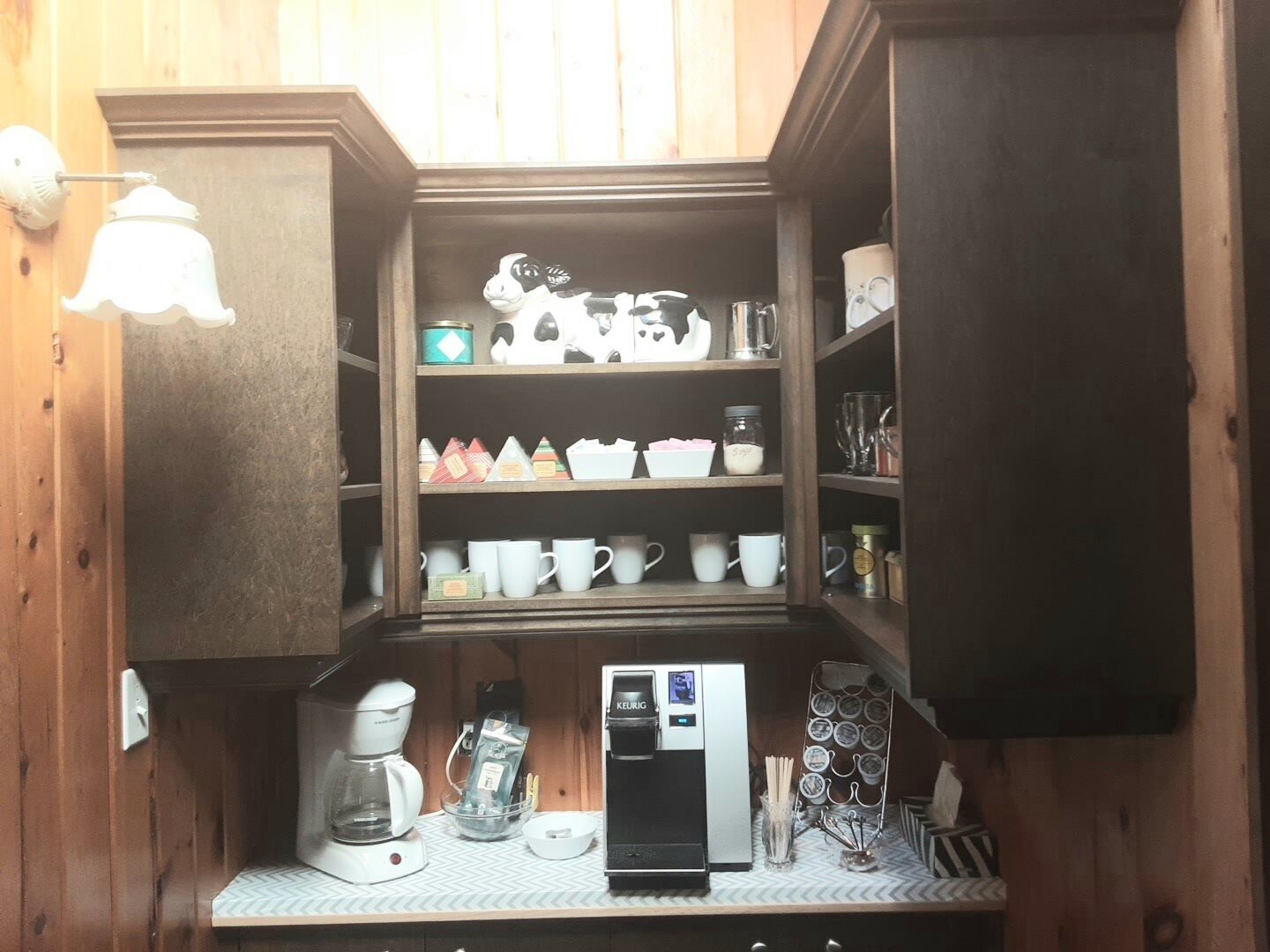 Cocina compacta con armarios de madera, cafetera, máquina de café Keurig y diverso menaje de cocina.