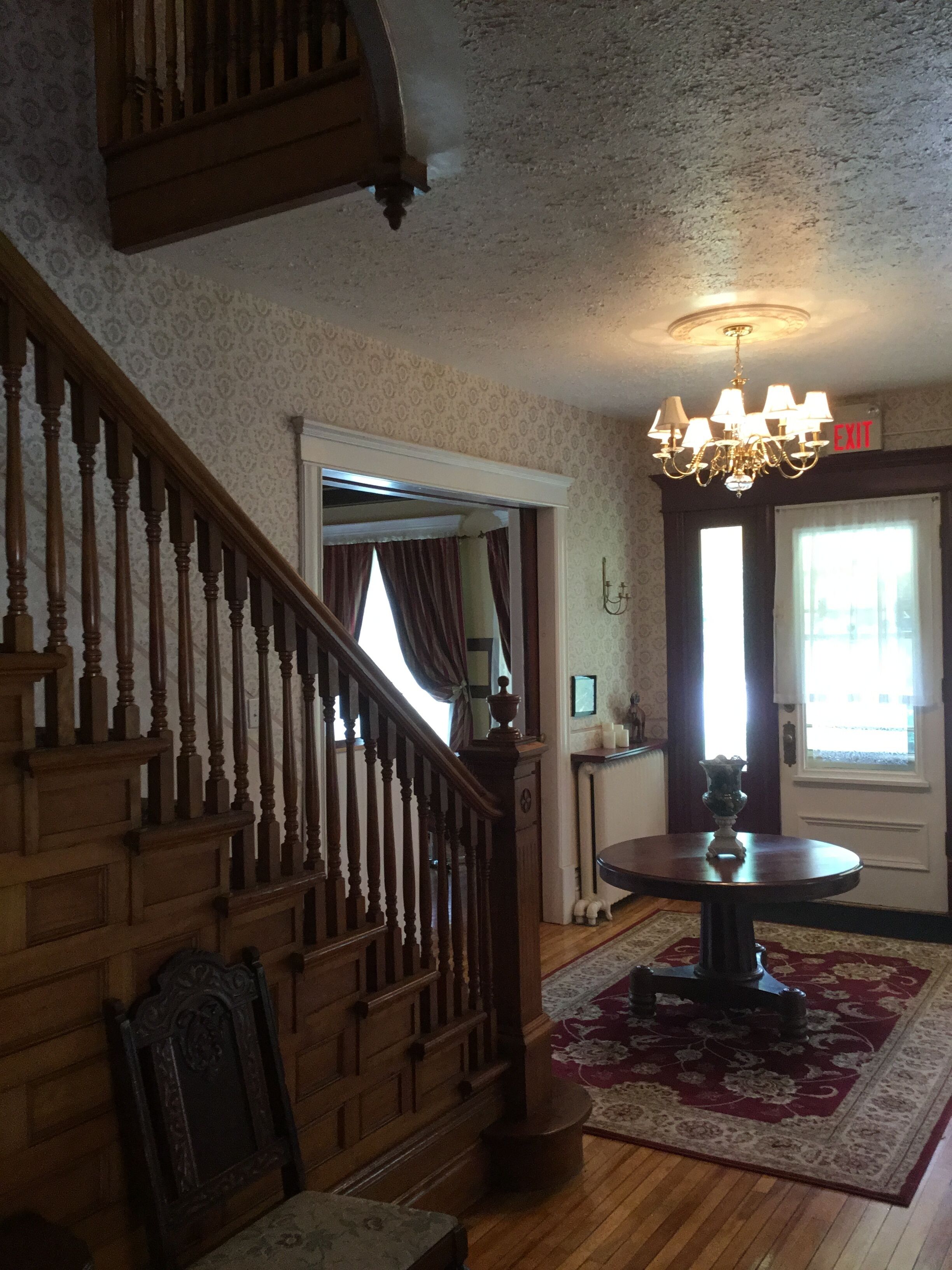 A staircase with wooden balusters, a chandelier, and a patterned rug in a room with a door marked "EXIT".
