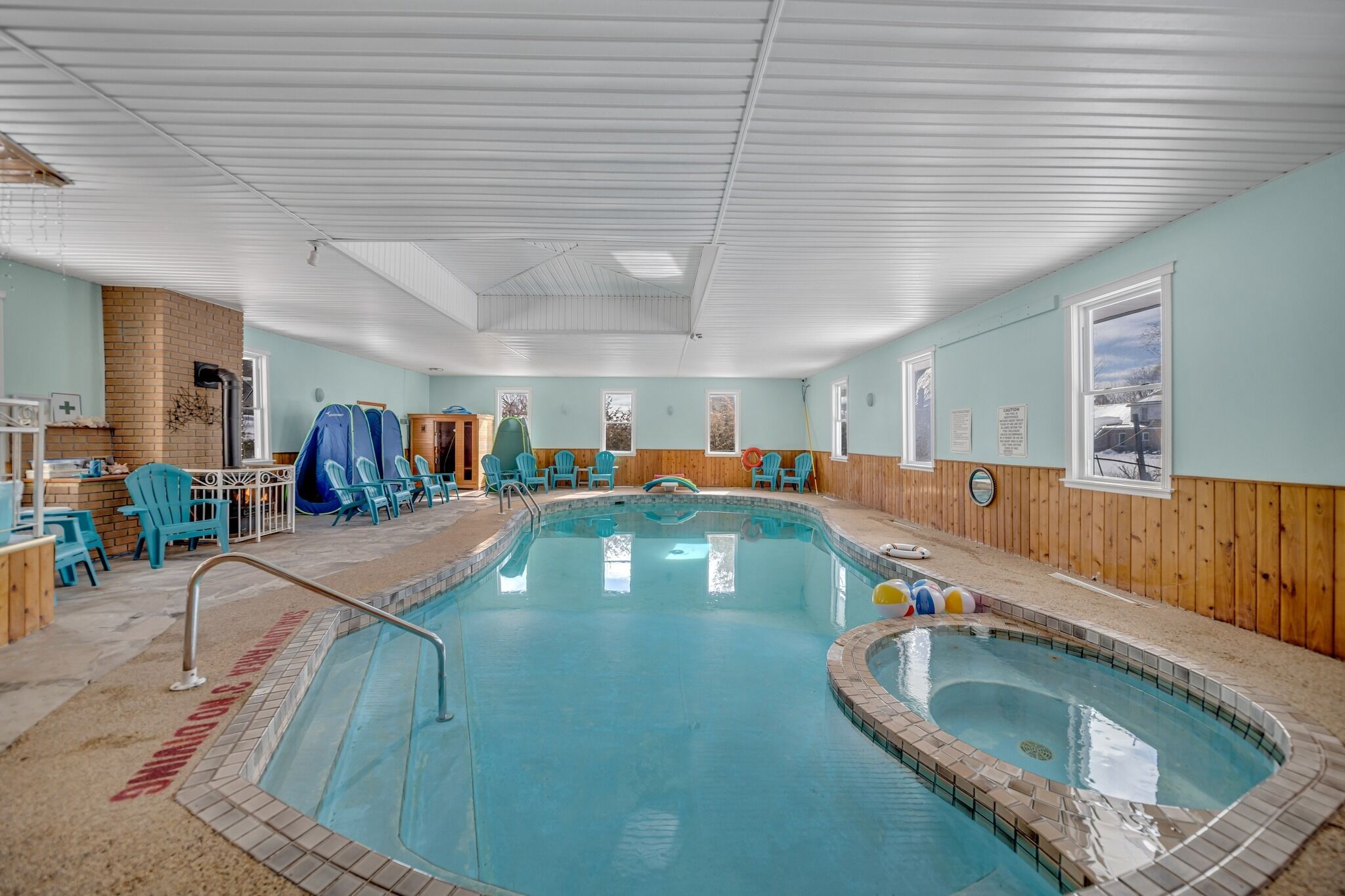 An indoor swimming pool with blue chairs and a small hot tub.
