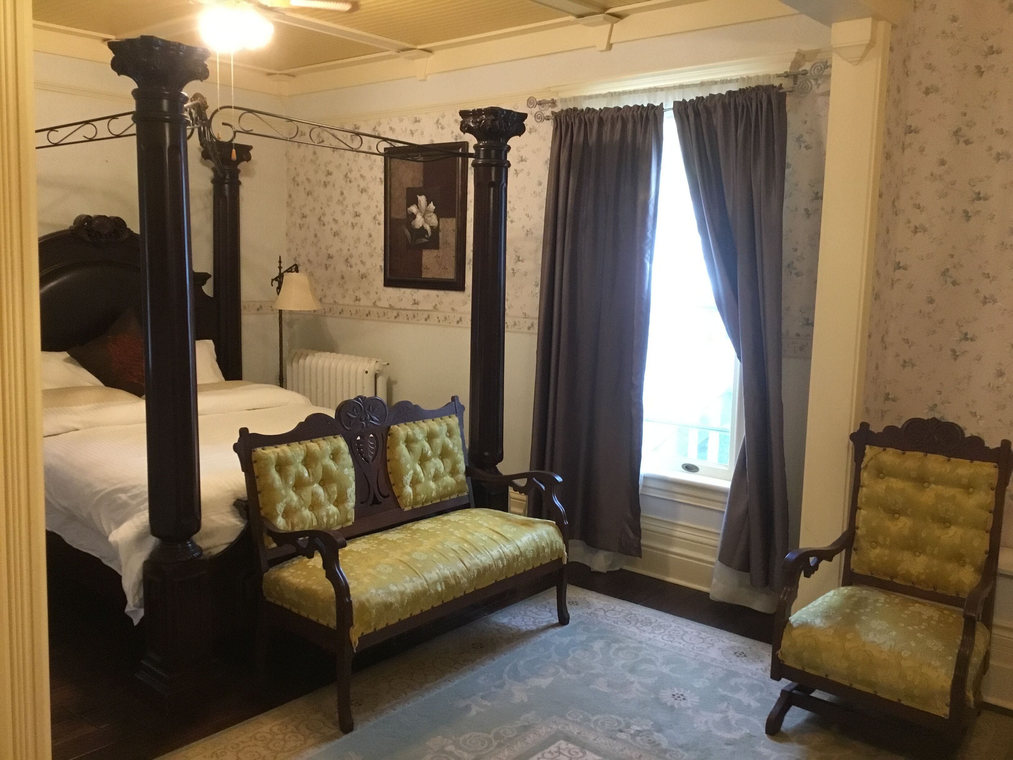 Ein Schlafzimmer mit einem Himmelbett, einer hölzernen Bank und einem Sessel.