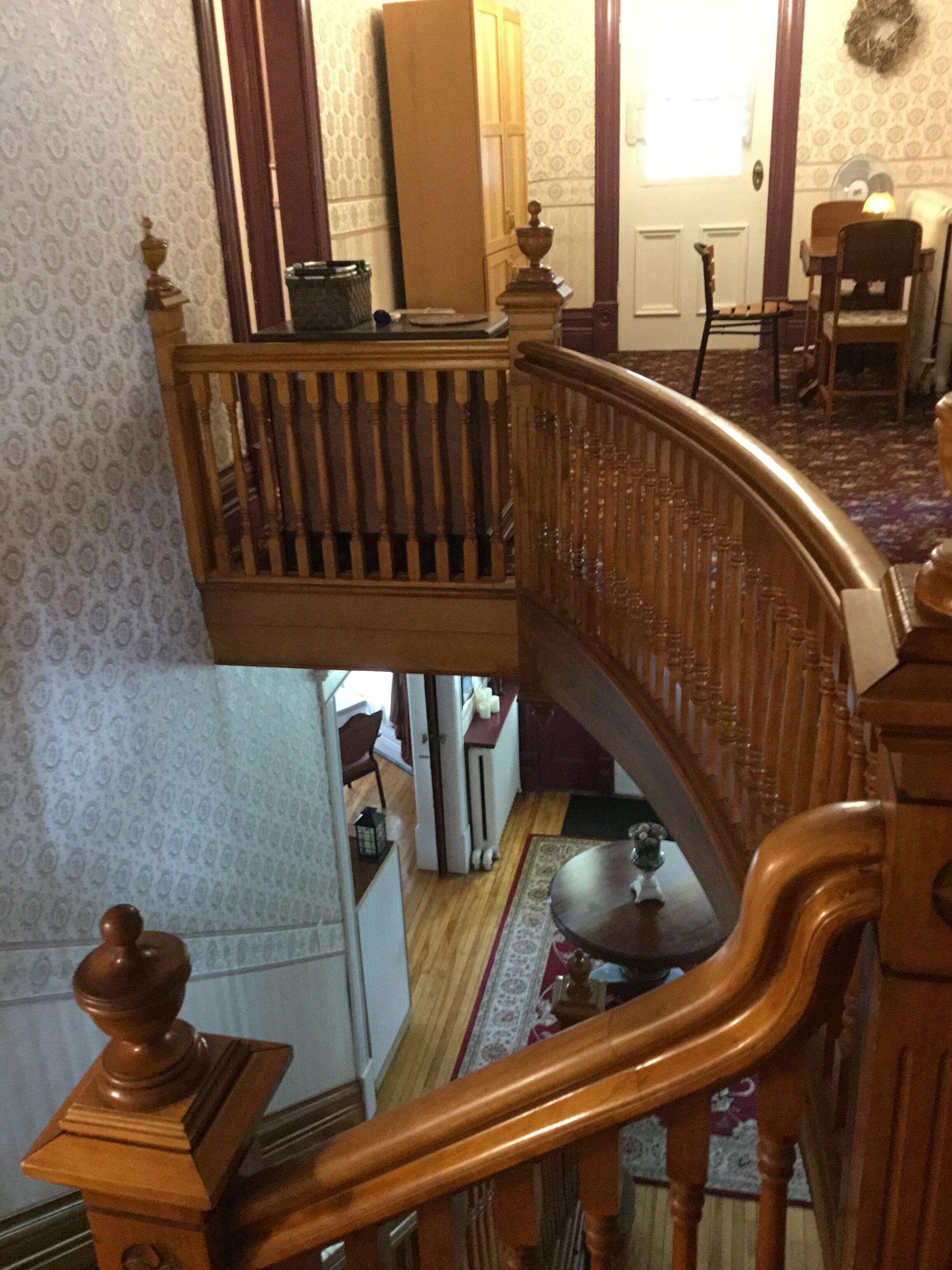 A multi-level wooden staircase with a railing, a dining area with a table and chairs, and a patterned wallpaper on the walls.