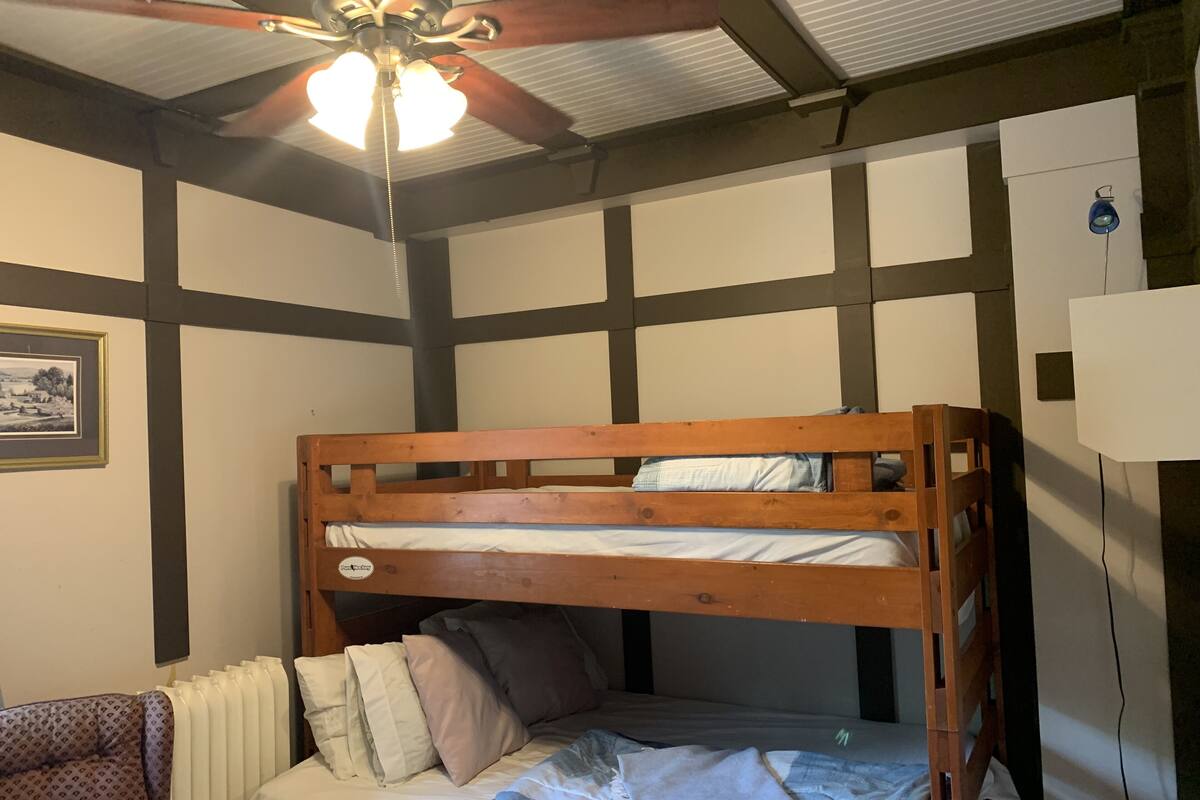 Un lit superposé avec une structure en bois, du linge de lit blanc et un ventilateur de plafond.