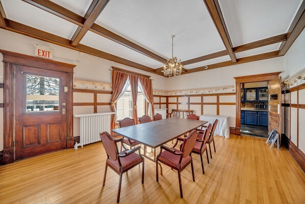 A conference room with a long table and chairs, wooden floors, a chandelier, and an exit sign. - Marmora and Lake Inn (Marmora and Lake)