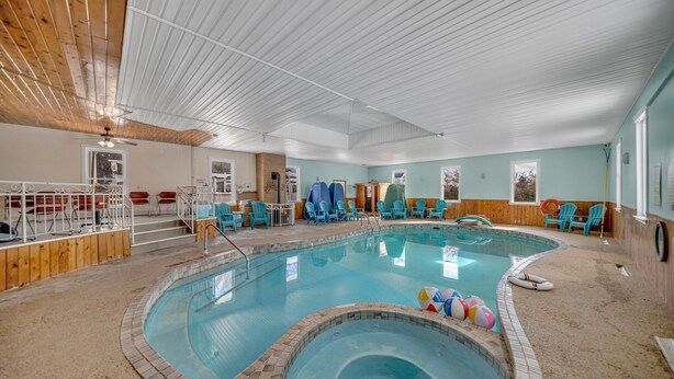 Een binnenzwembad met betegelde rand, omringd door blauwe stoelen, een kleine jacuzzi en een houten terras.