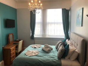 A bedroom with a bed, a dresser, a television, a chandelier, and a window with curtains. - Atlantis (Torquay)