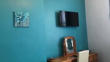 Un dormitorio con paredes color turquesa, una cama con toallas blancas, un aparador de madera, un espejo y un televisor de pantalla plana montado en la pared.