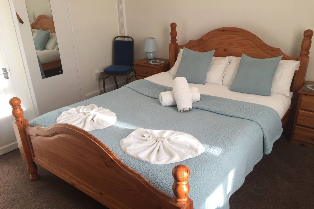Una cama bien hecha con cabecera de madera, una manta azul y dos toallas blancas dobladas sobre la cama.