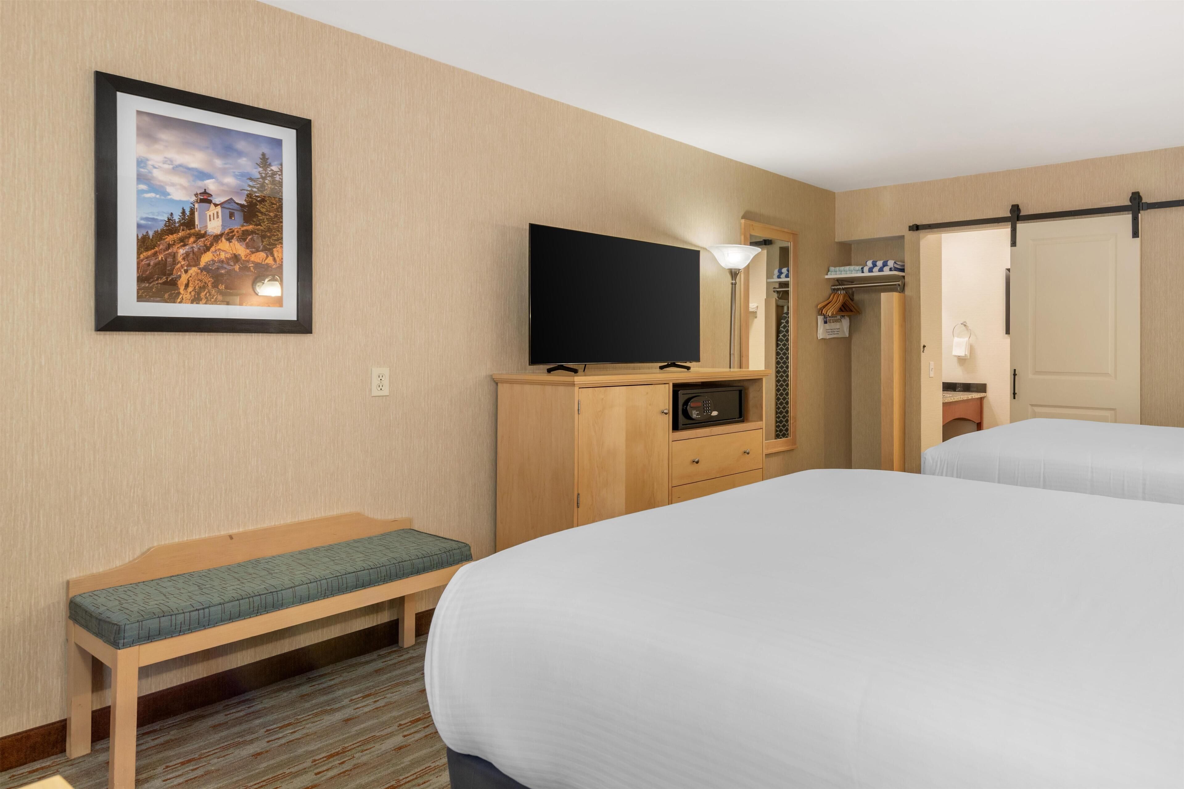 A hotel room with a bed, a bench, a television, and a framed picture on the wall.