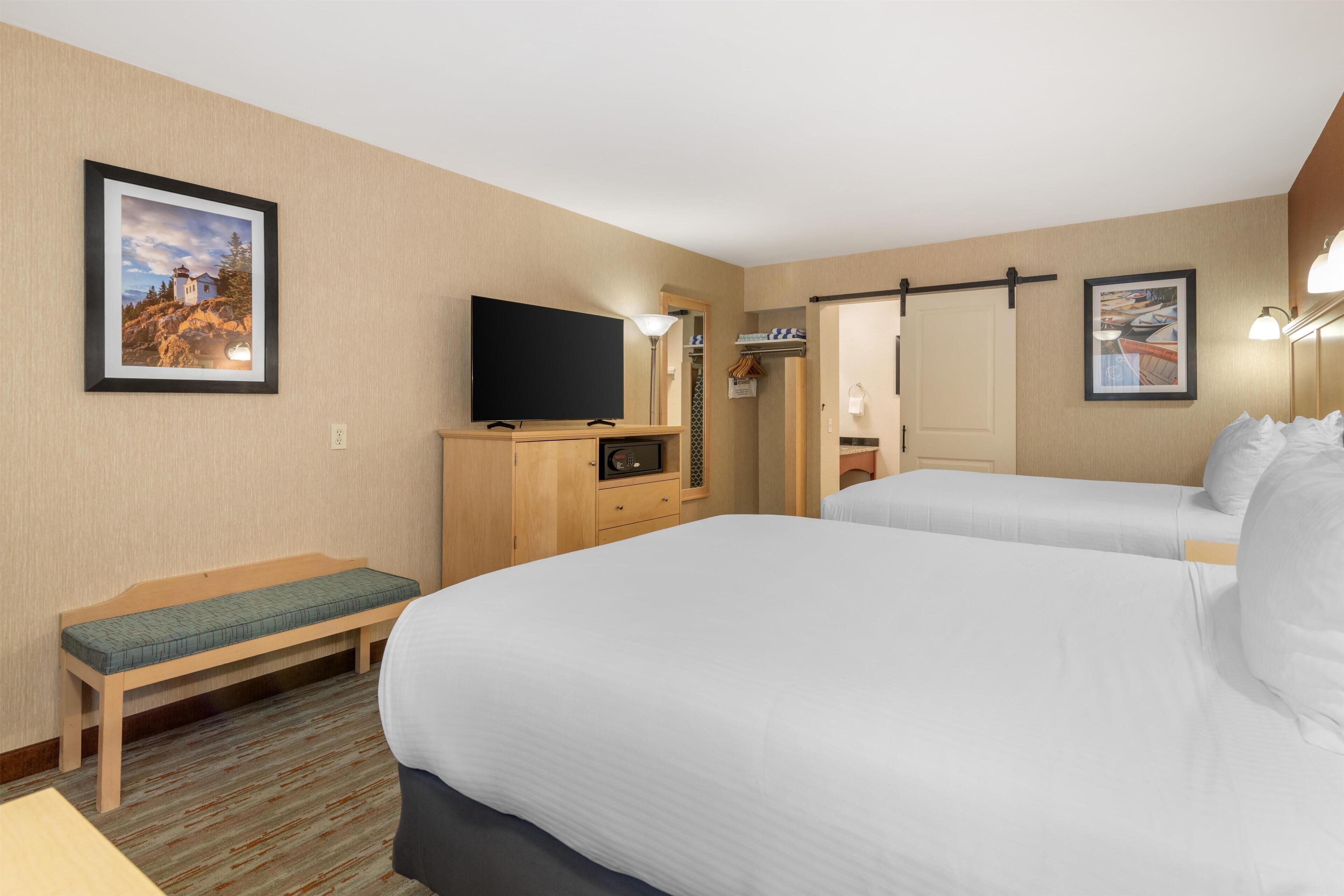 A hotel room with two beds, a TV, a bench, and framed pictures on the walls.