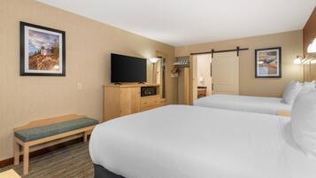 A hotel room with two beds, a TV, a bench, and framed pictures on the walls.