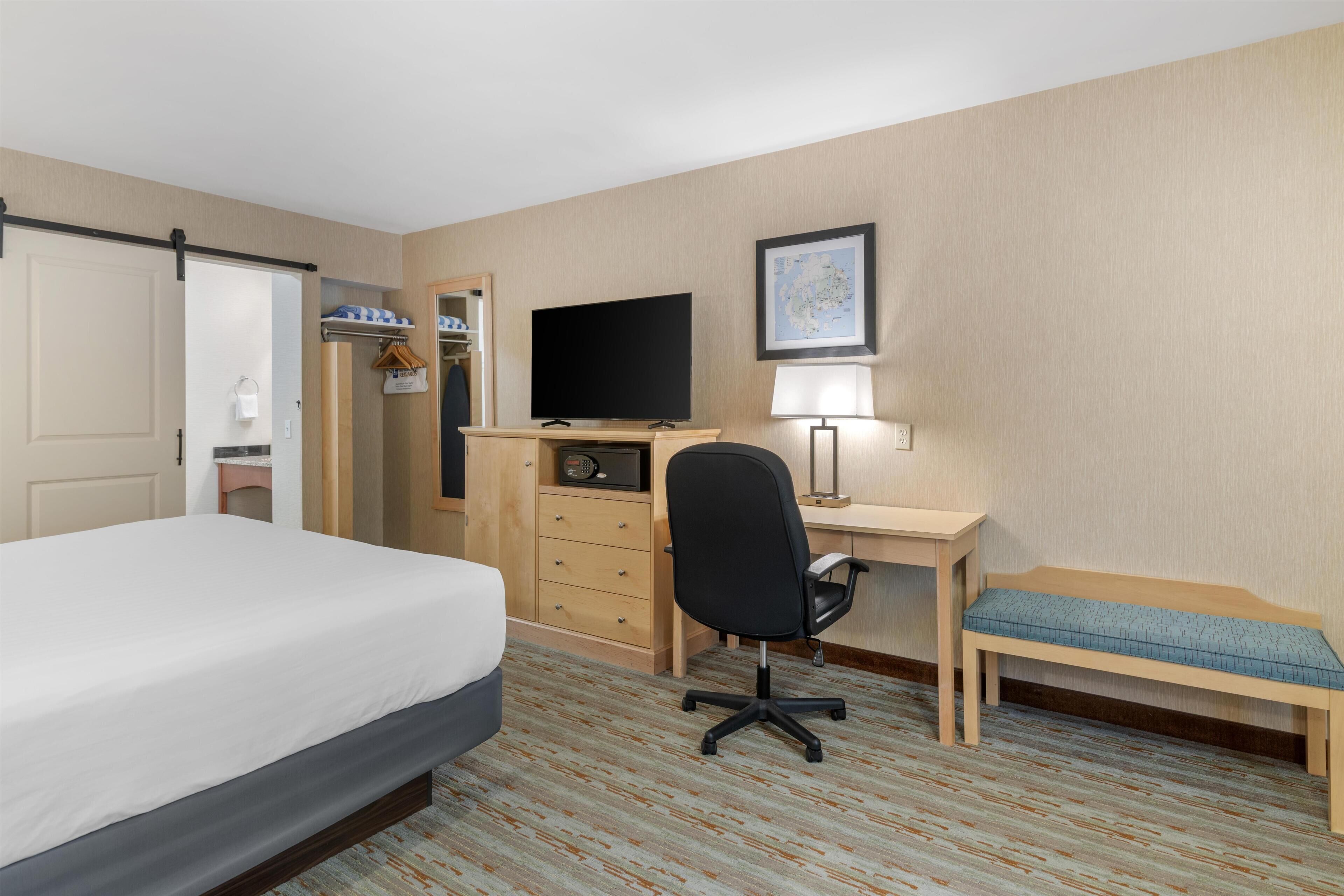 A hotel room with a bed, desk, chair, television, and a map on the wall.