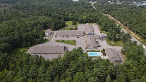 Une vue aérienne d’un vaste complexe de bâtiments entouré d’une forêt dense, avec plusieurs aires de stationnement et une piscine.