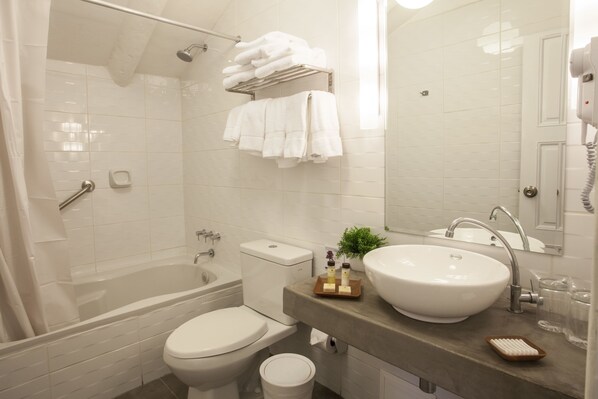 Un baño moderno con bañera, inodoro y lavamanos. Hay toallas en un perchero, una planta pequeña y artículos de tocador en la encimera.