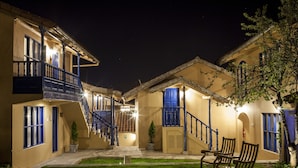 A courtyard with a staircase leading to a balcony, surrounded by buildings with blue accents and potted plants.