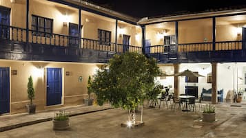 Un patio con un árbol central, varios balcones y mobiliario de exterior.