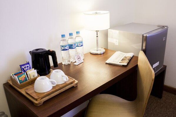 A hotel room desk with a coffee maker, water bottles, a lamp, a refrigerator, and a tray with cups and snacks. - Tierra Viva Cusco San Blas (Cusco)
