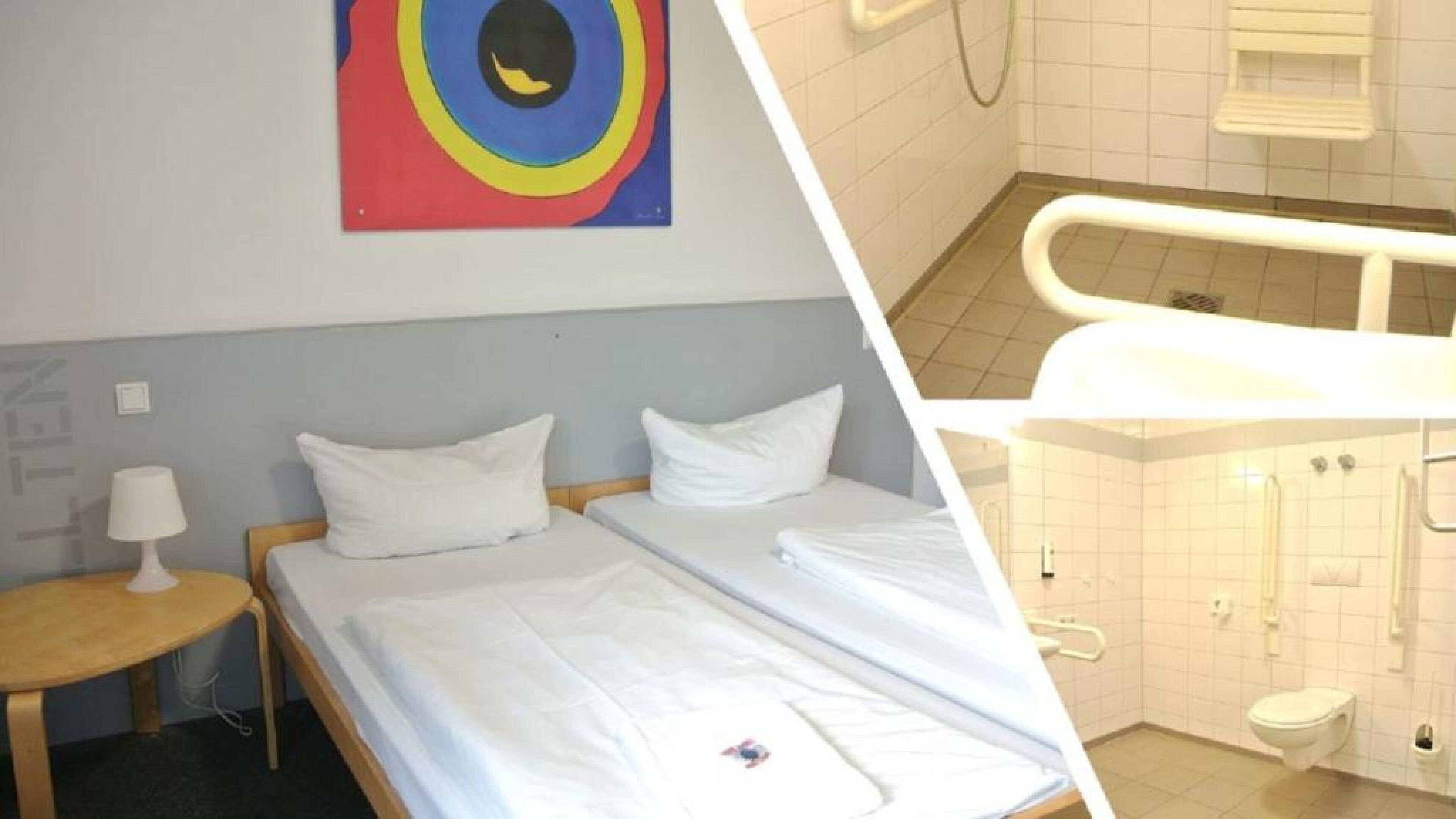 A room with two beds, a small table with a lamp, and a colorful painting on the wall.