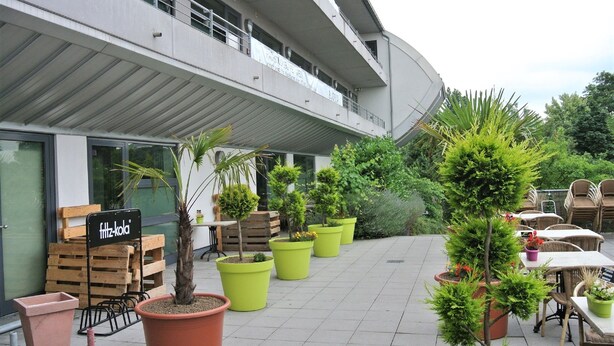 Un espace extérieur aménagé en terrasse, avec des plantes en pot, du mobilier de jardin et un panneau indiquant « fritz-kola ».