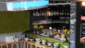 Un espace bar agrémenté d’un mur végétal, d’étagères remplies de bouteilles et de verres, ainsi que d’un tableau affichant la carte des boissons.