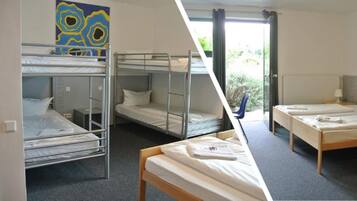 A dormitory room with bunk beds, a small desk, and a window with curtains.