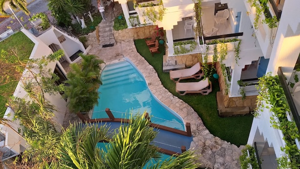 A swimming pool surrounded by lounge chairs, a stone pathway, and lush greenery. - Hotel Labnah (Playa del Carmen)