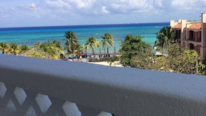 A coastal view with a clear sky, turquoise sea, palm trees, and a building with a red roof. - Hotel Labnah (Playa del Carmen)