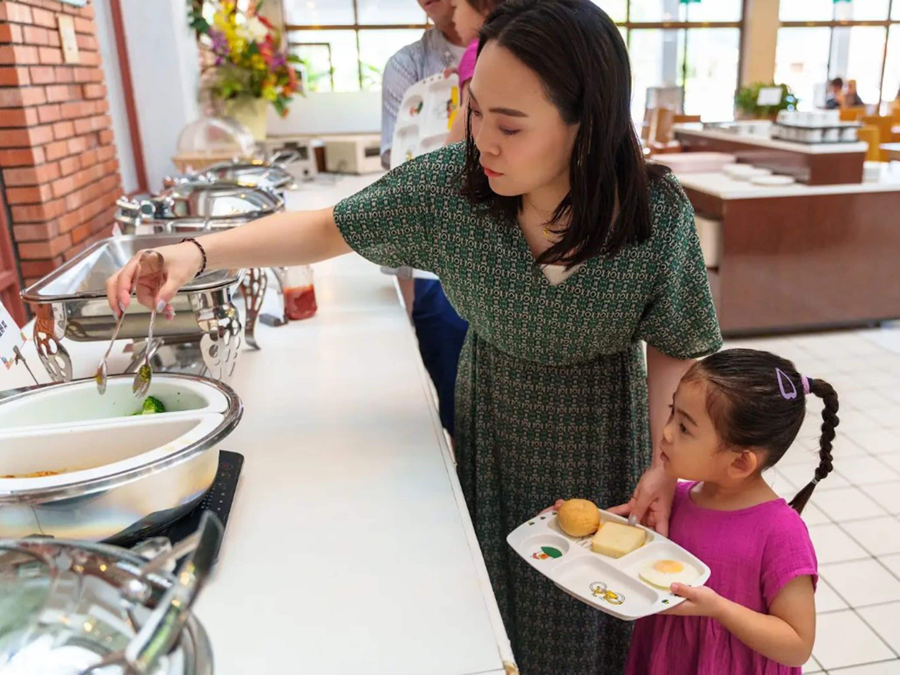 A buffet setup with multiple serving stations, a person serving food, and a child holding a tray with food items.