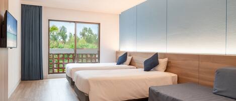 A modern hotel room with two beds, a sofa, a TV, and a balcony with a view of greenery.