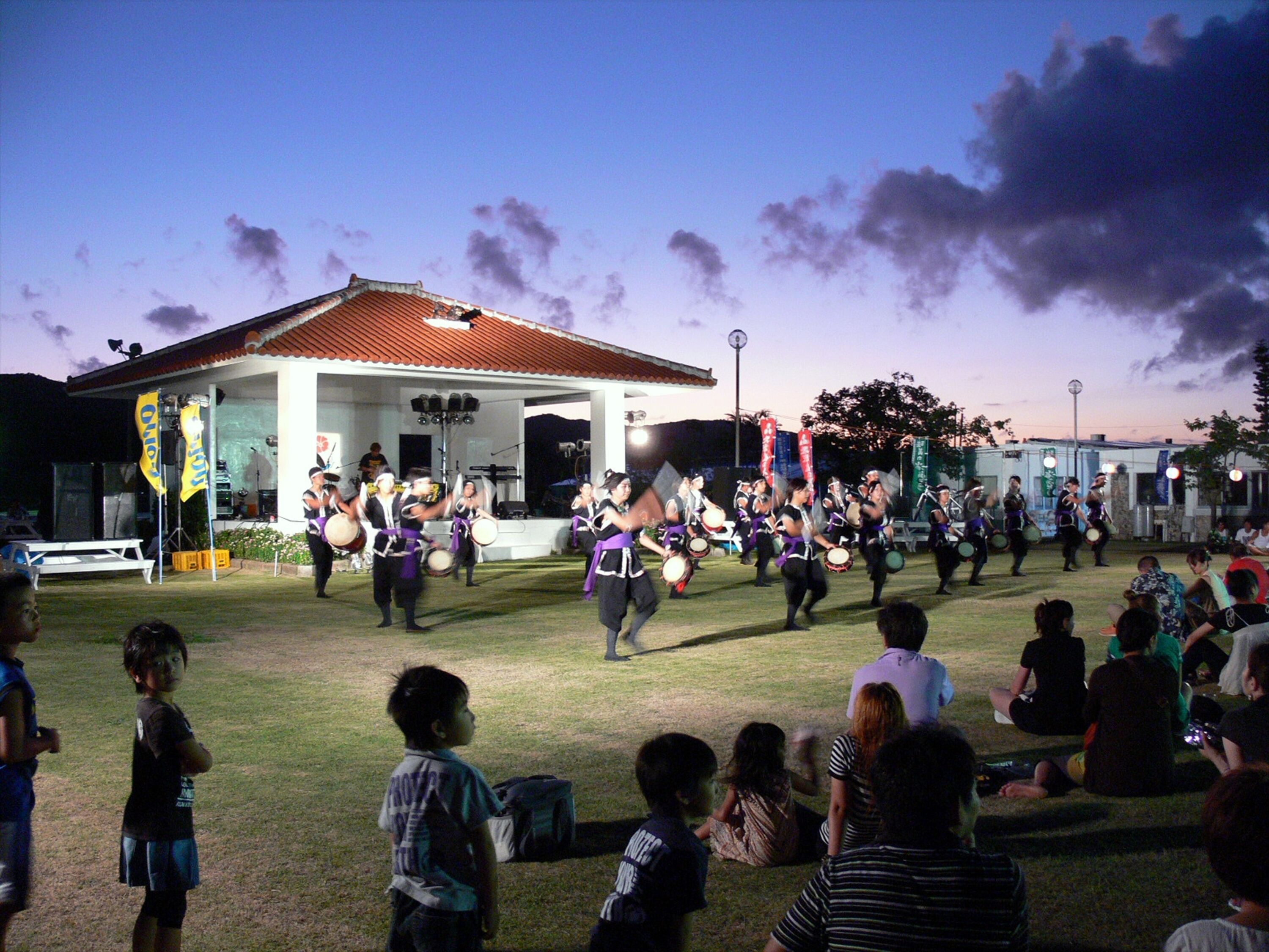 A group of people performing a traditional dance in an outdoor setting with a building in the background.
