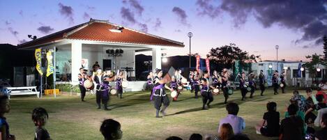 A group of people performing a traditional dance in an outdoor setting with a building in the background.