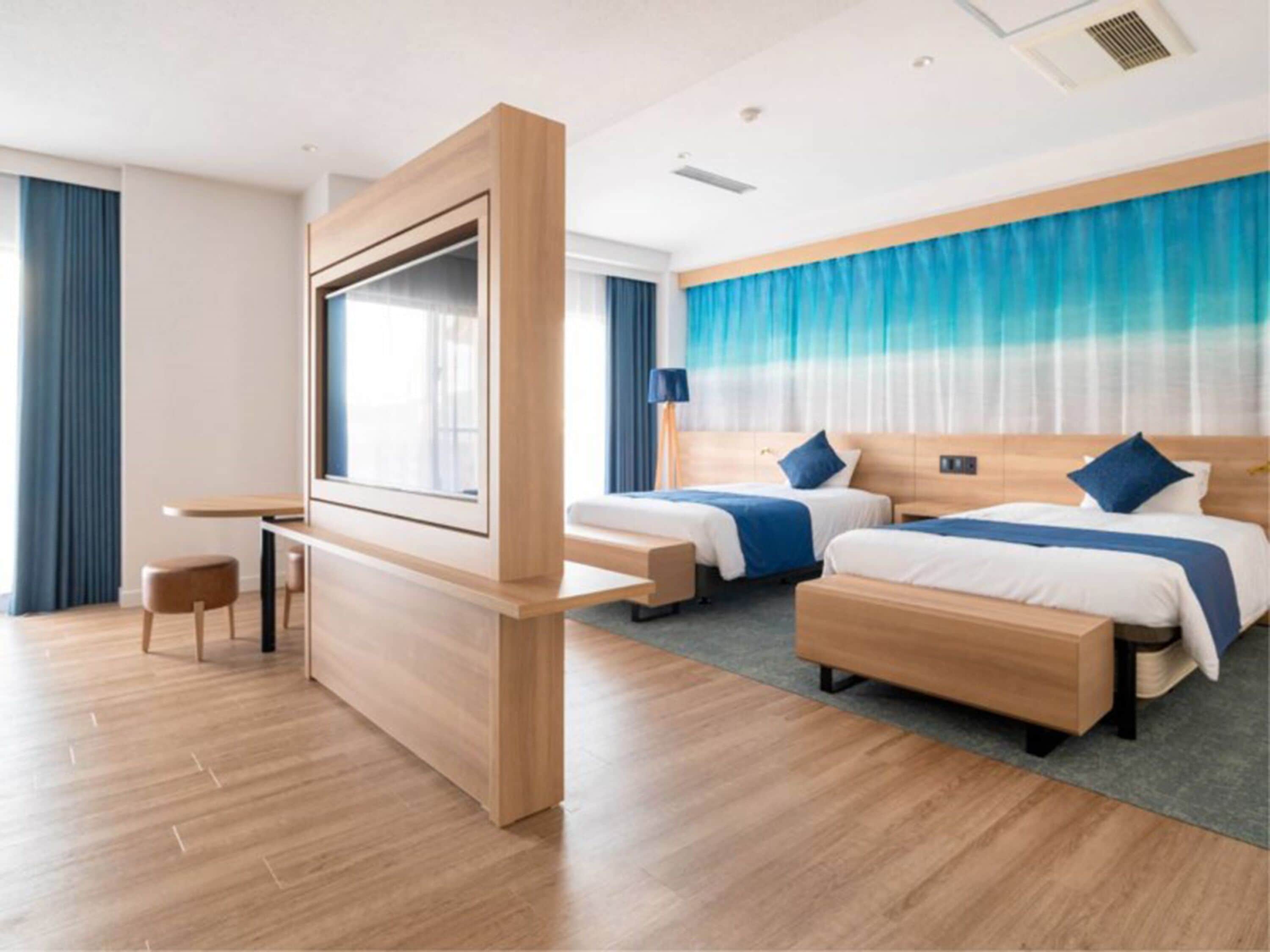 A modern hotel room with two beds, a desk, and a TV.