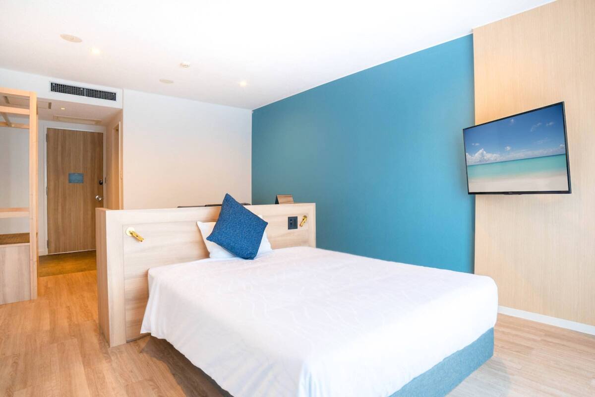 Une chambre moderne avec un grand lit, un mur d’accent bleu et un téléviseur fixé au mur.