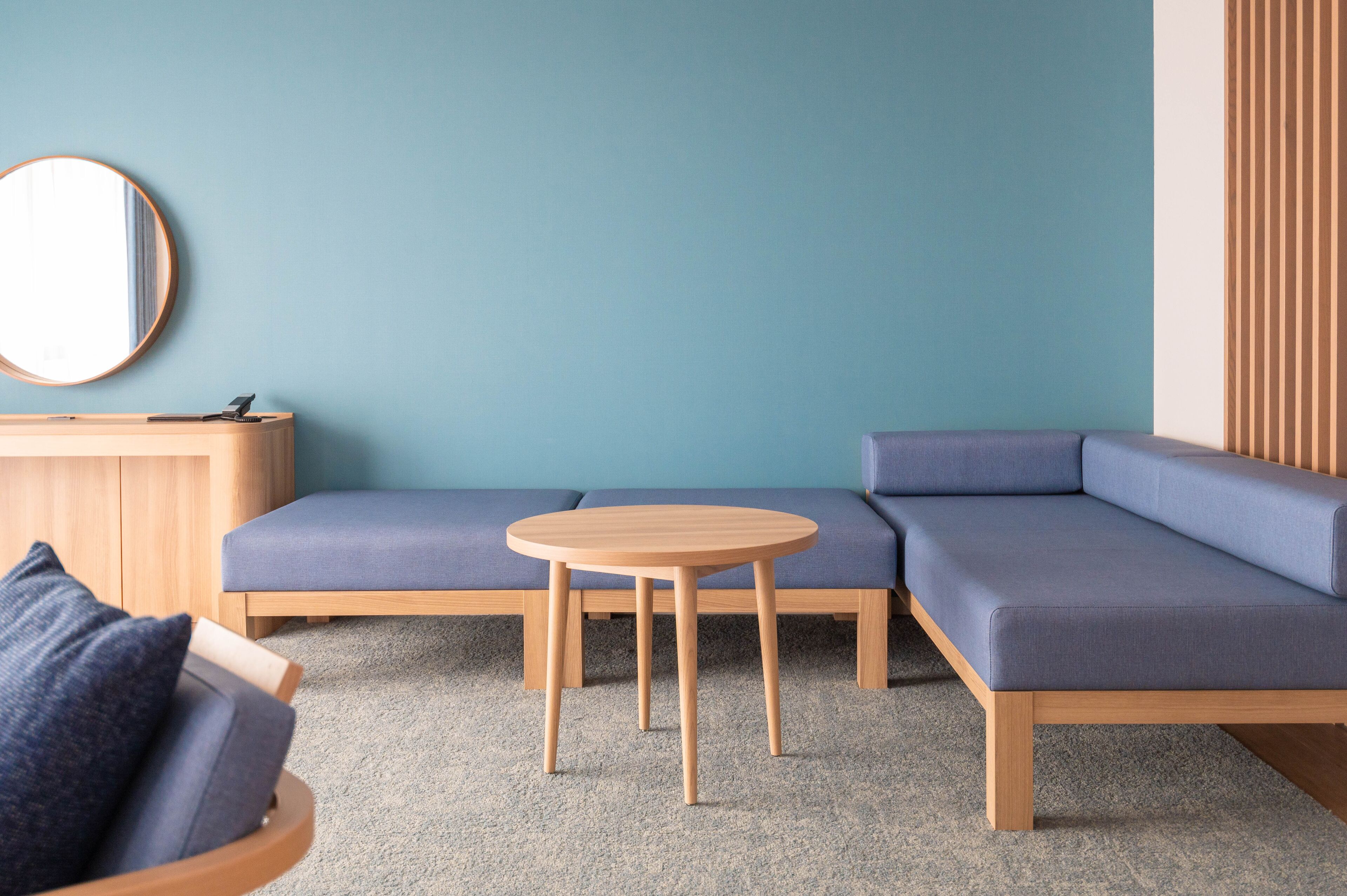 A modern living room with a sectional sofa, a round wooden table, and a round mirror on the wall.