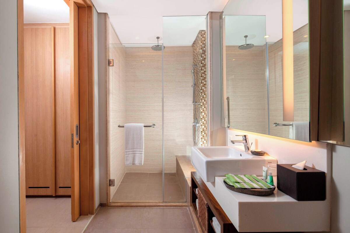 A modern bathroom with a glass shower enclosure, a wooden door, a white sink, and a mirror.