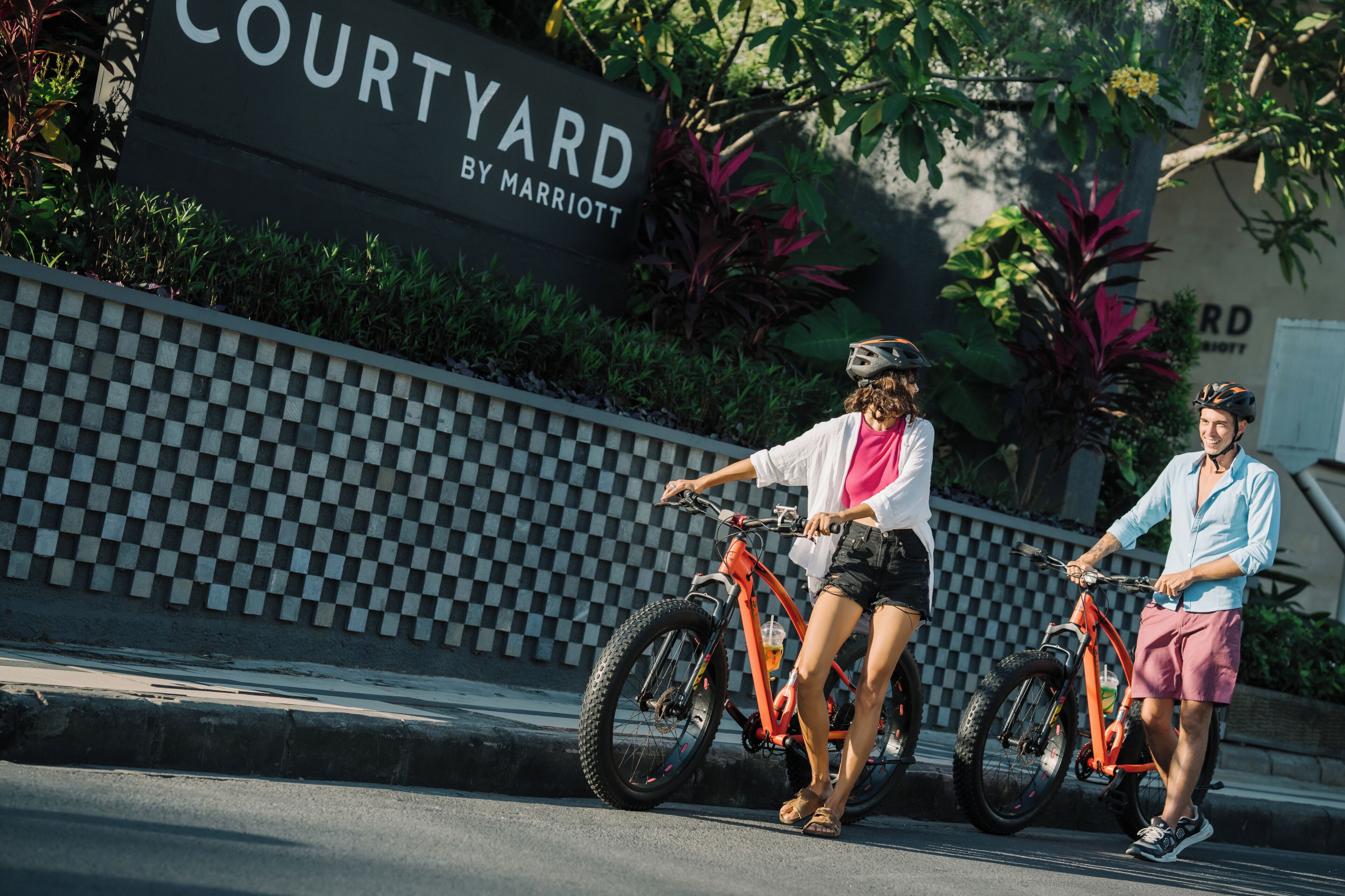 Two people on bicycles in front of a sign that reads 'COURTYARD BY MARRIOTT.'