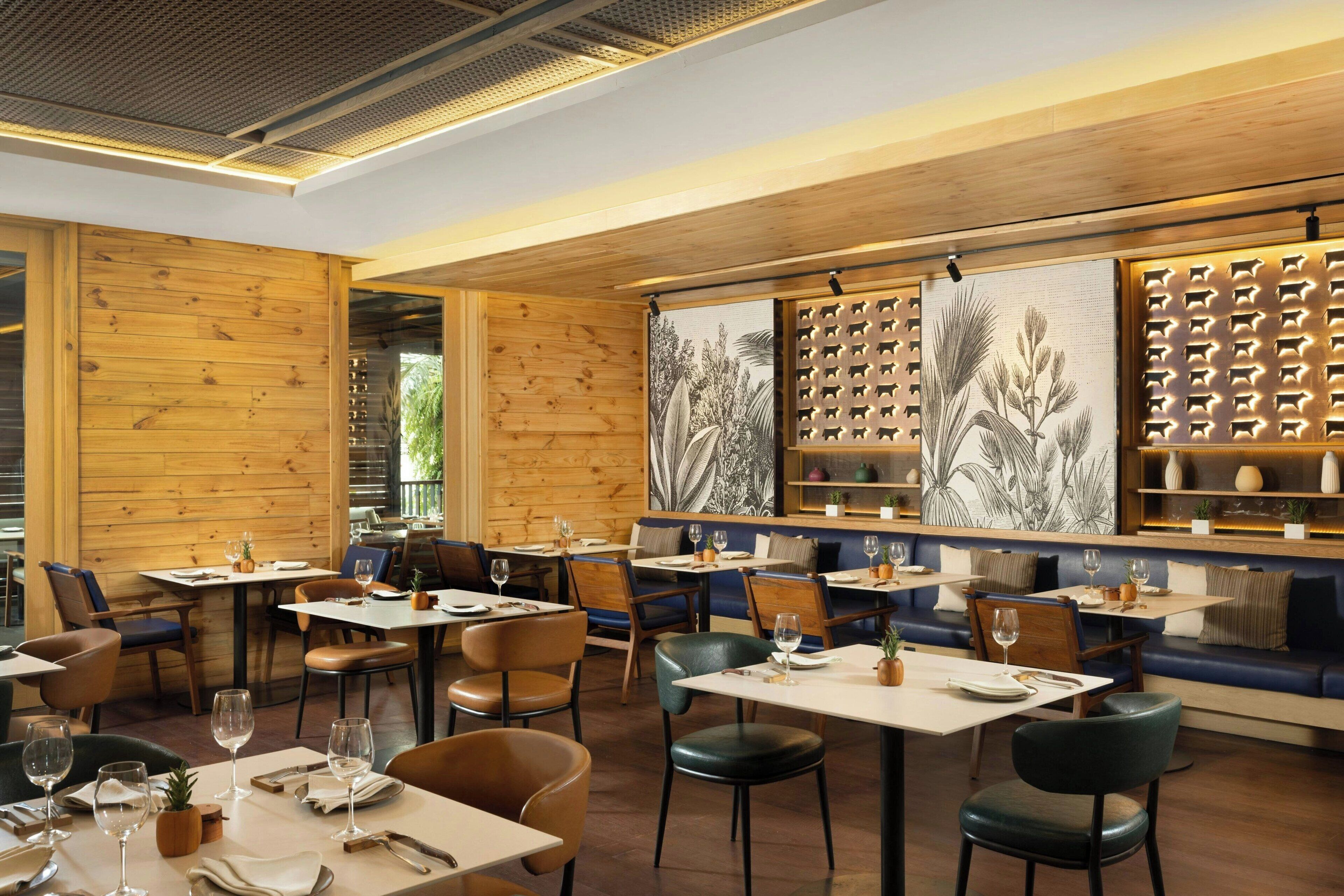 Restaurante com paredes de painel de madeira, mesas com cadeiras e área de bar com prateleiras.