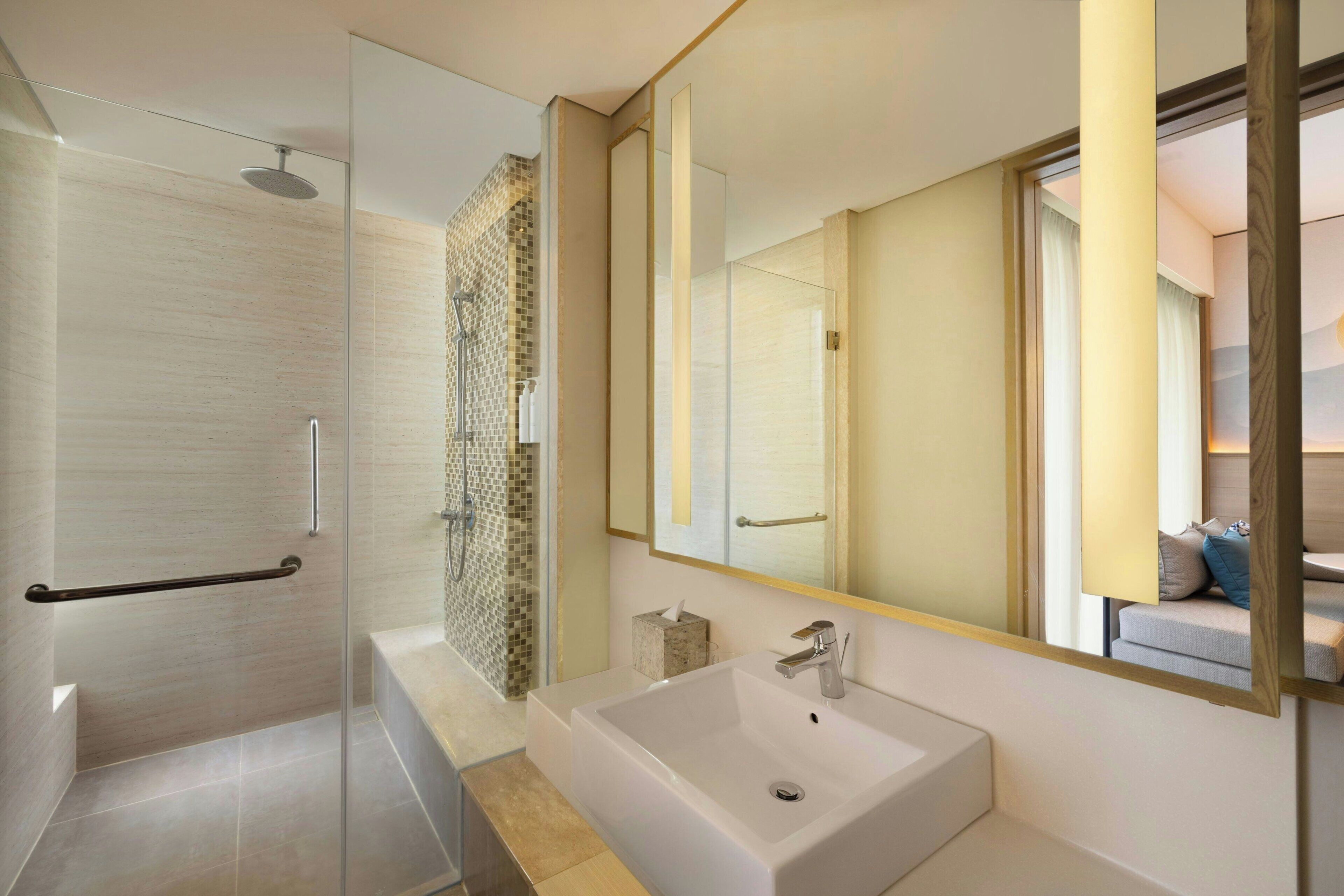 Un baño moderno con cabina de ducha de vidrio, un espejo grande y un lavamanos blanco.