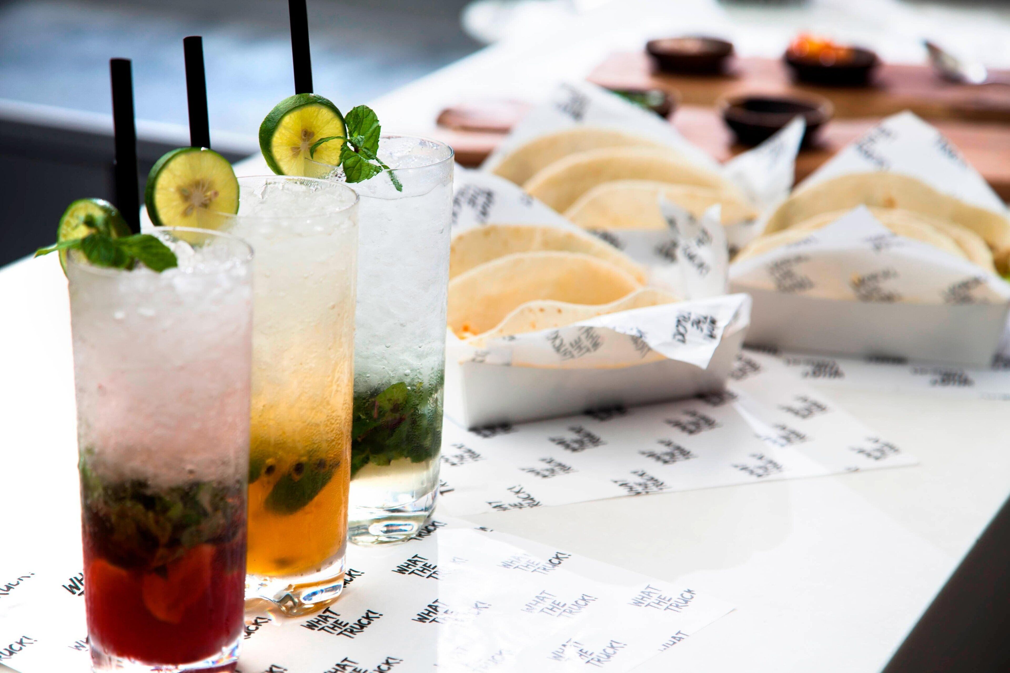 Tres bebidas heladas con pajitas y adornos, un menú con texto y tacos sobre una mesa.