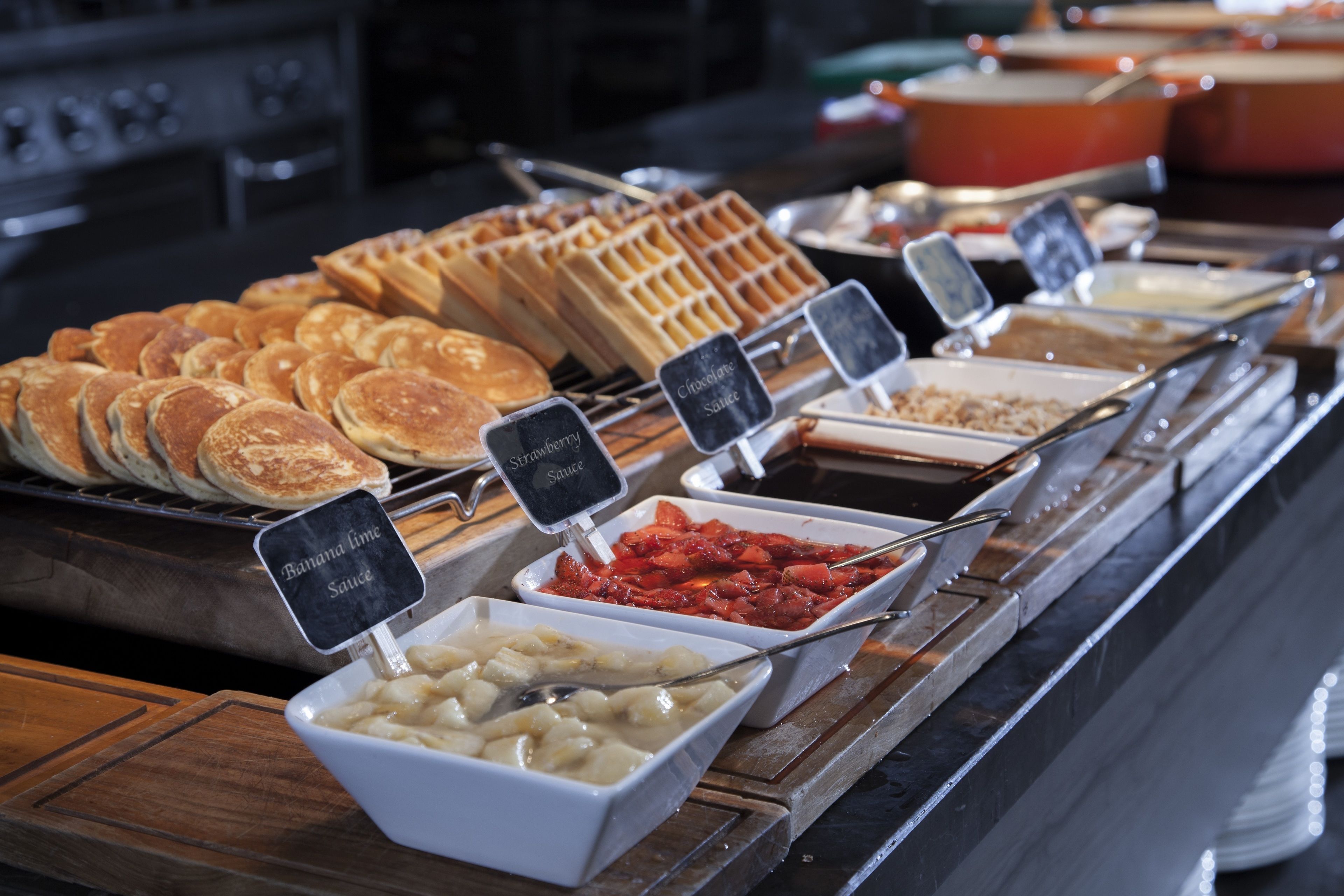 Un buffet proposant une variété de plats, notamment des gaufres, des crêpes et différentes sauces.