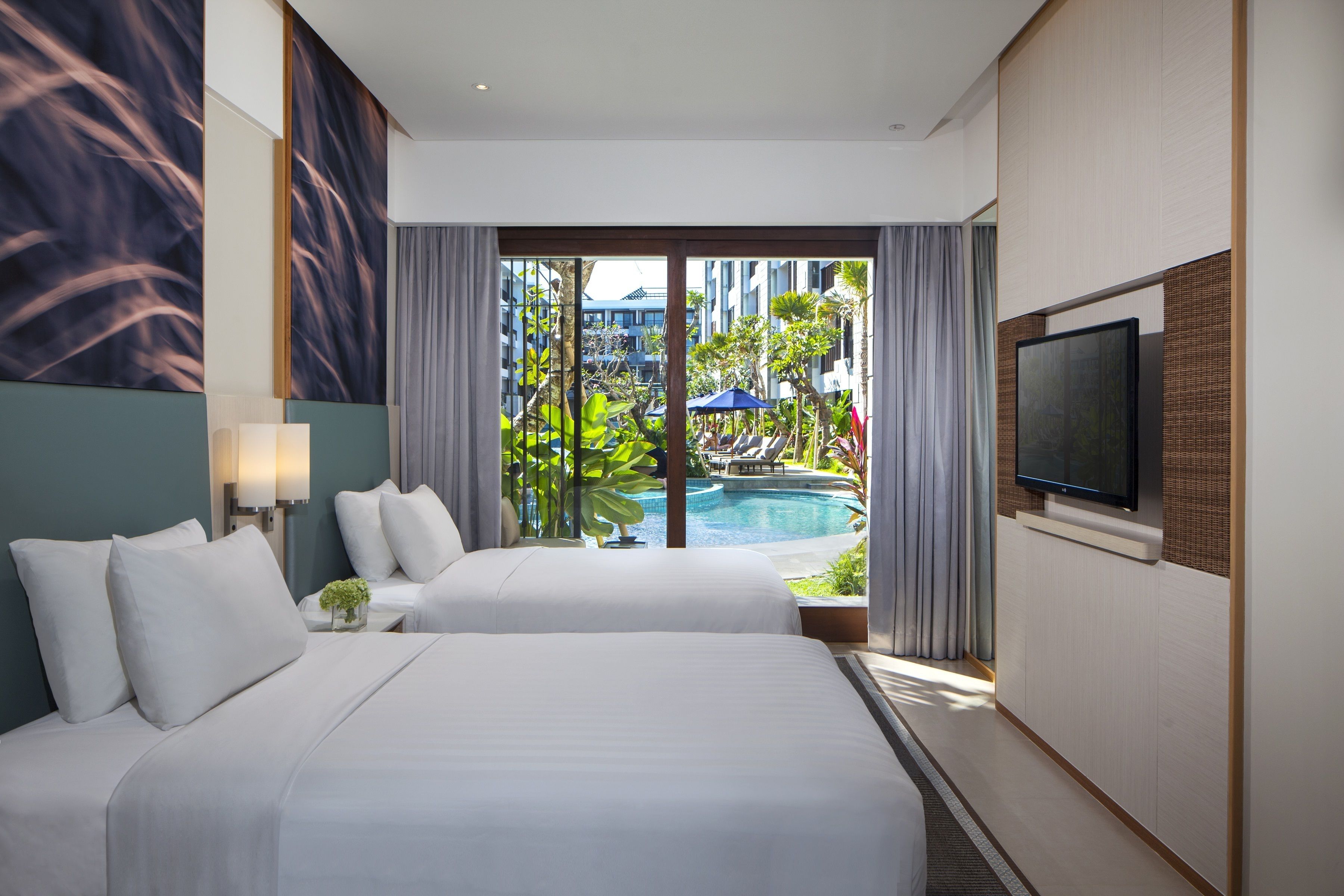 A hotel room with two beds, a TV, and a view of a swimming pool and greenery.