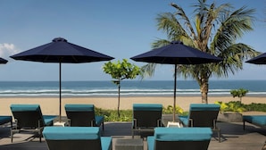 Area relax in spiaggia con sedie in vimini e ombrelloni blu scuro, con vista sull'oceano.