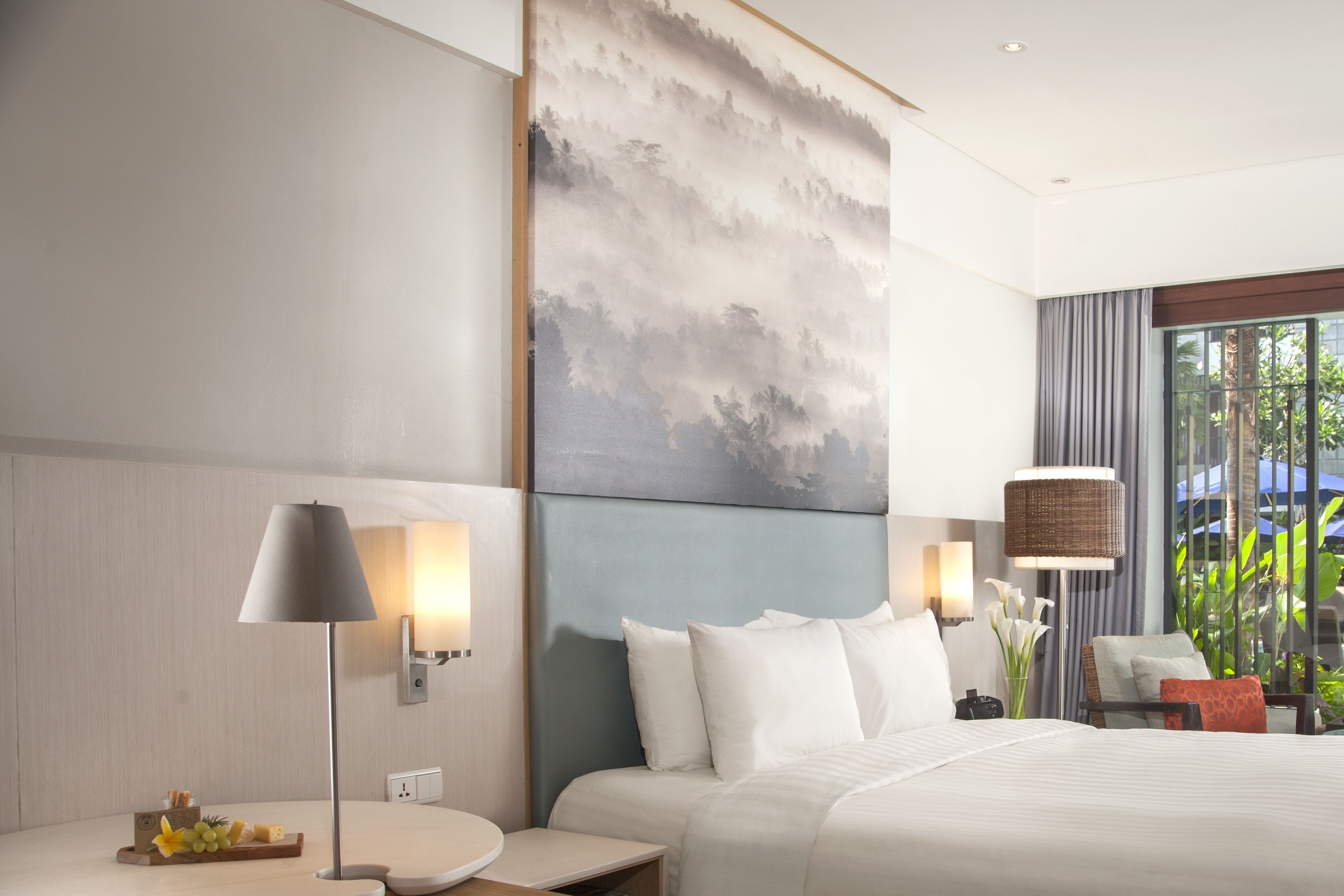 Una habitación de hotel moderna con una cama grande, dos mesitas de noche, una lámpara de pared y vistas a zonas verdes por la ventana.