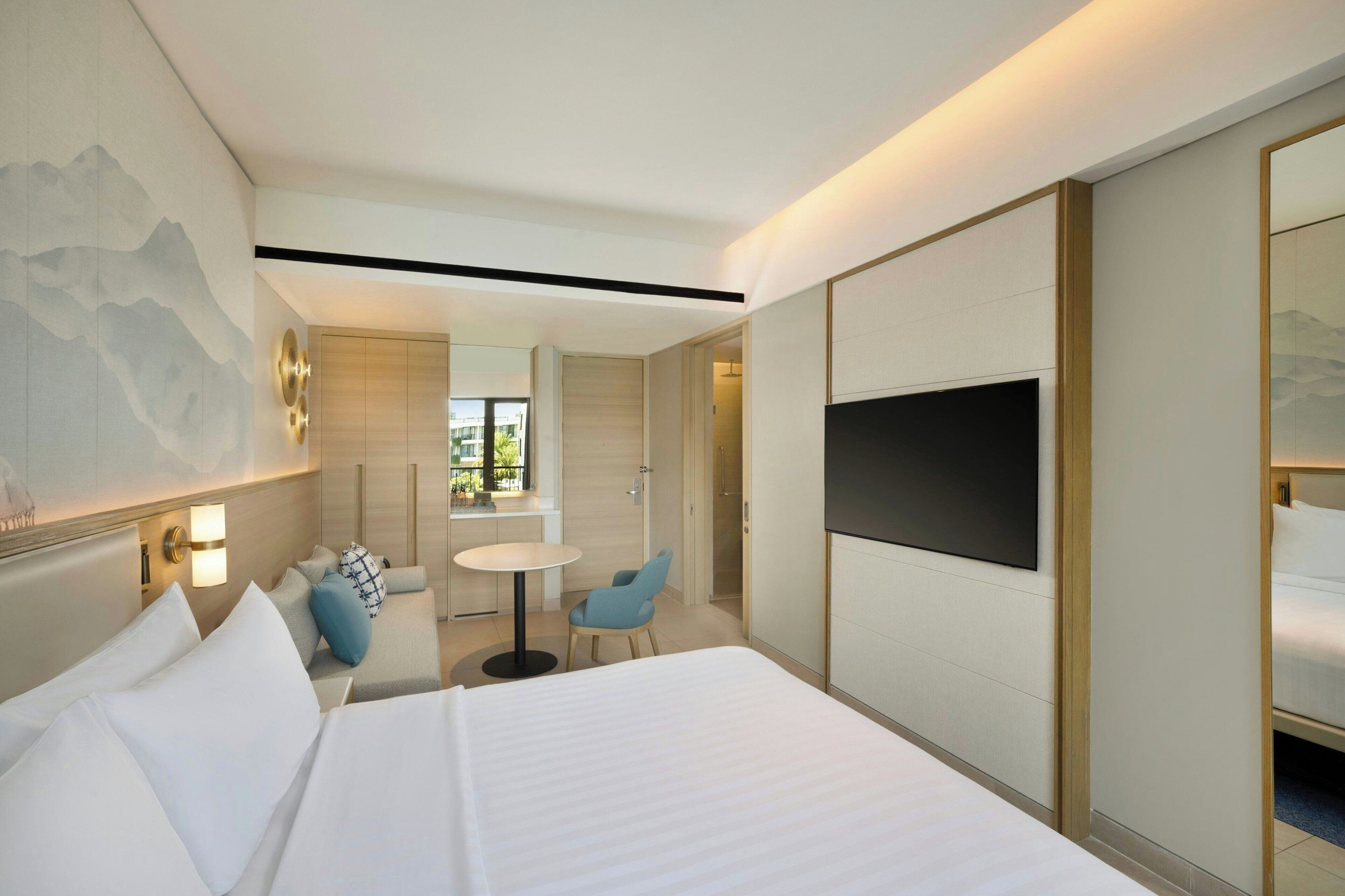 A hotel room with a large bed, a TV, a desk, and a view of the outdoors.