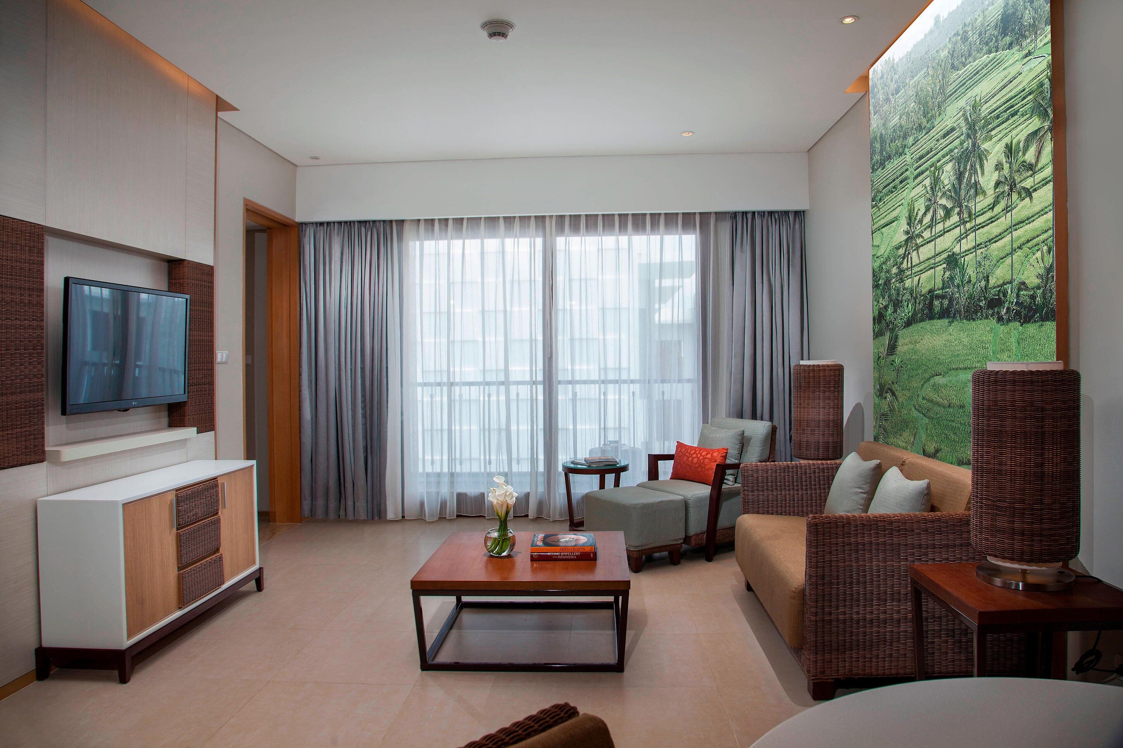 A modern living room with a flat-screen TV, a sofa, a coffee table, and a large painting of a landscape.