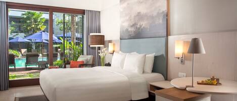 A modern hotel room with a large bed, a bedside table with a lamp, a view of the pool area, and a painting on the wall.