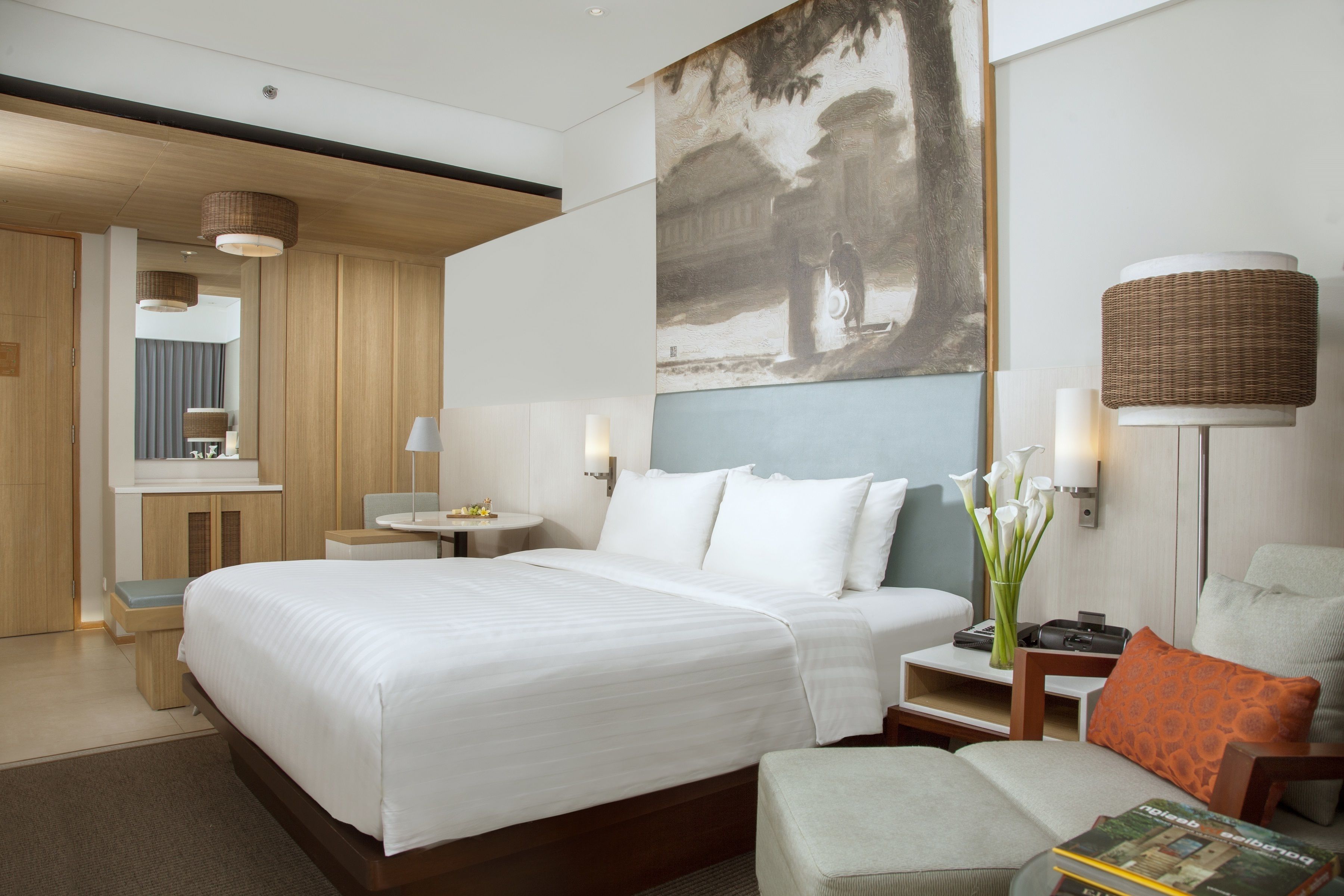 Habitación de hotel con una cama grande, una mesita de noche, una pequeña mesa, una silla y un cuadro en la pared.