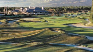 A golf course with bunkers, a clubhouse, and a large building in the background. - Club Wyndham Dye Villas (North Myrtle Beach)